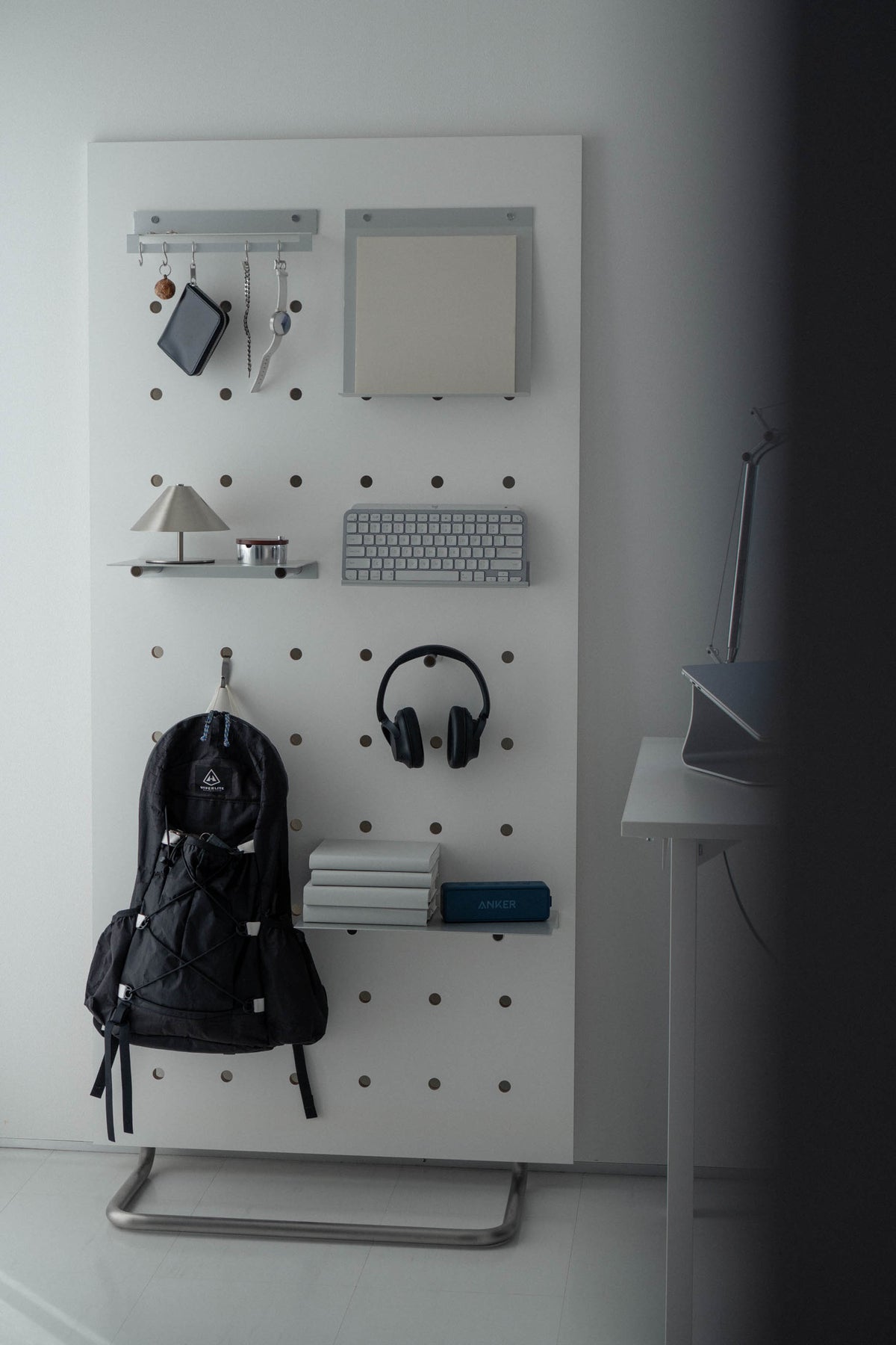 Pure White のボードに、キーボードやヘッドホン、バックパックを掛けたデスクまわり
