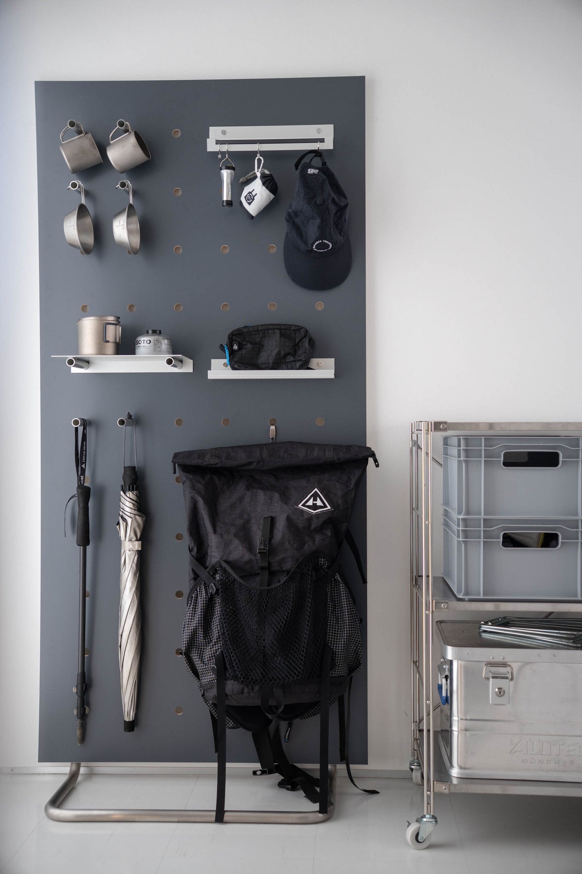 Deep Gray のボードに、マグや帽子、バックパックを掛けたアウトドアの道具
